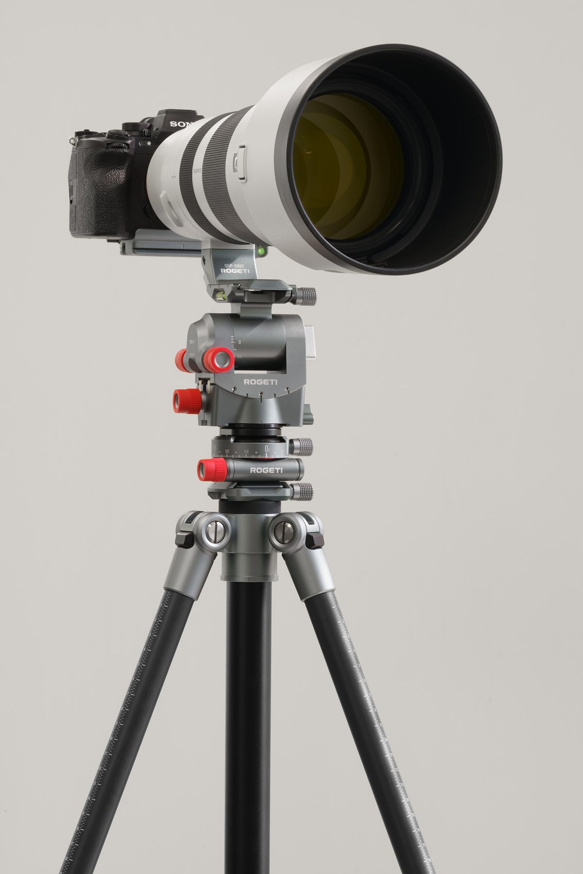 A camera with a large white and black telephoto lens mounted on ROGETI RG-1 Gear head, GZA panning head and T32 Lite Plus tripod. 